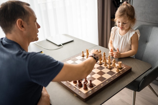 Father teaching his little daughter to play chess at the table in home kitchen the concept early chi
