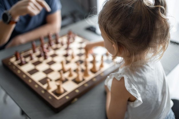 Фото Отец учит свою маленькую дочь играть в шахматы за столом на домашней кухне. концепция развития и образования детей в раннем возрасте. семейный досуг, общение и отдых.