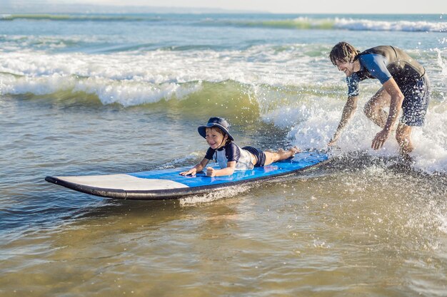 父は彼の幼い息子に休暇や休日に海でサーフィンする方法を教えています。子供と旅行とスポーツのコンセプト