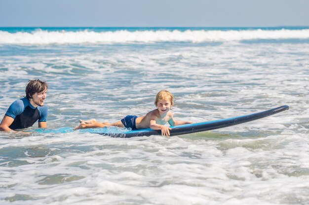 Father teaching his young son how to surf in the sea on vacation or holiday. Travel and sports with children concept