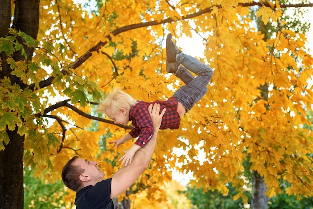 Father throws up his blond son Yellow leaves on background Family concept