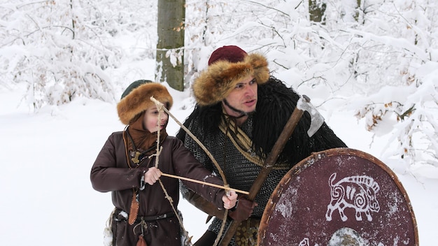 Father viking teach his son to archery in the winter forest