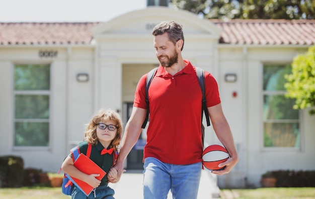 Father walking son to school parent and pupil of primary school schoolboy with backpack