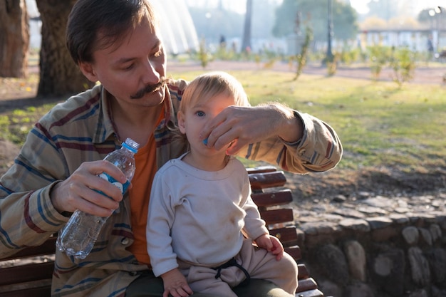 Foto padre che innaffia un bambino su una panchina del parco durante il tramonto