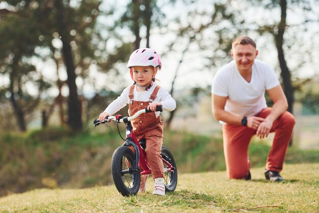 Father in white shirt teaching daughter how to ride bicycle outdoors