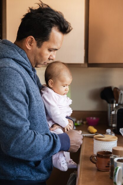 朝、両親と家族の概念でコーヒーを作るキッチンで女の赤ちゃんを持つ父親