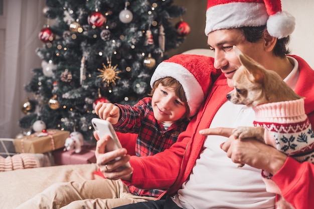 Padre con bambino e cucciolo il giorno di natale con lo smartphone