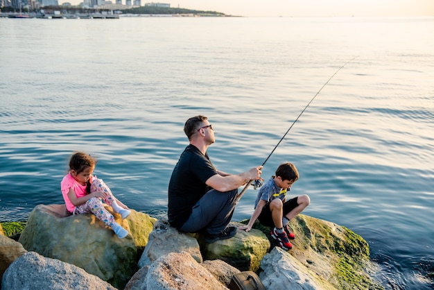 Father with children on a fishing trip by the sea Children fish over a cliff in the sea