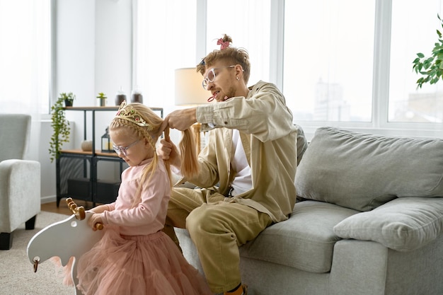 Father with crazy hairstyle and mad face grimace making hair for daughter, happy parenting