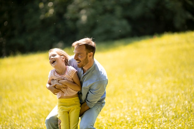 公園で芝生の上で楽しんでいるかわいい小さな娘を持つ父