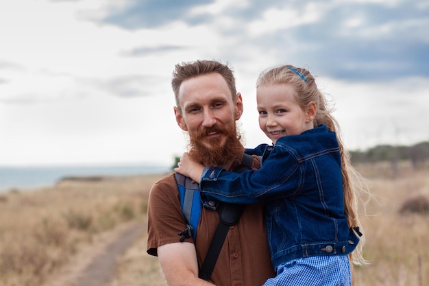 Father with daughter in hands standing on hill with nature lanscape Little blonde girl smiling and hugging dad outdoor