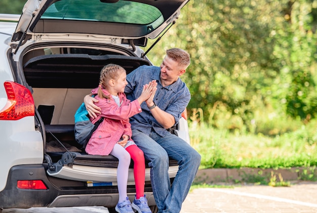 Father with daughter sitting on car trunk after schooling