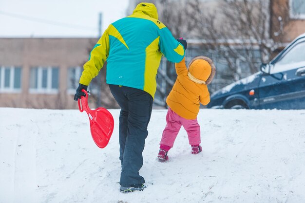 Father with daughter in yellow winter coats sliding snowed hill