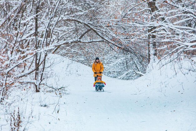 눈 덮인 언덕을 미끄러지는 노란 겨울 코트에 딸과 함께 아버지