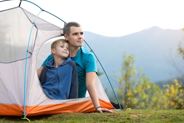 father with his child son resting together in a tent in summer mountains.