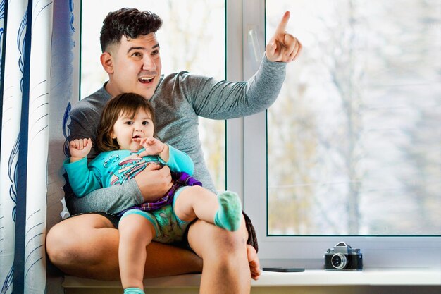 Photo father with his daughter playing sitting in a window taking a picture