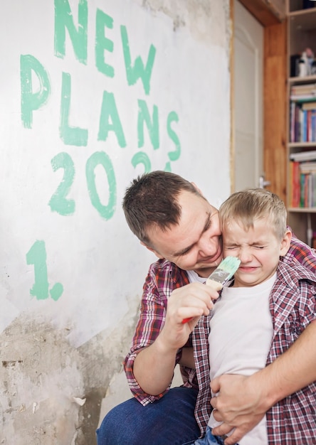 Photo father with kids repairing room together, unhanging wallpaper and planning new year on wall