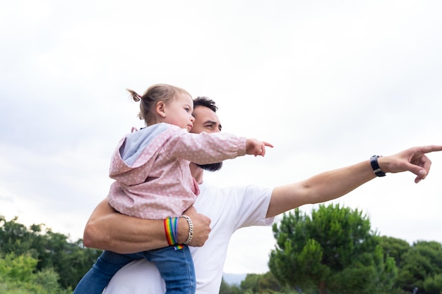 Father with lgbt bracelet pointing ahead holding a little girl