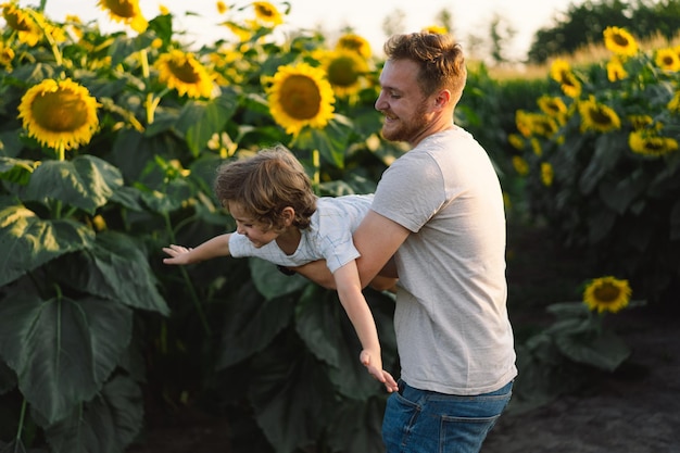 Foto padre con il figlio piccolo nel campo di girasoli durante l'ora d'oro