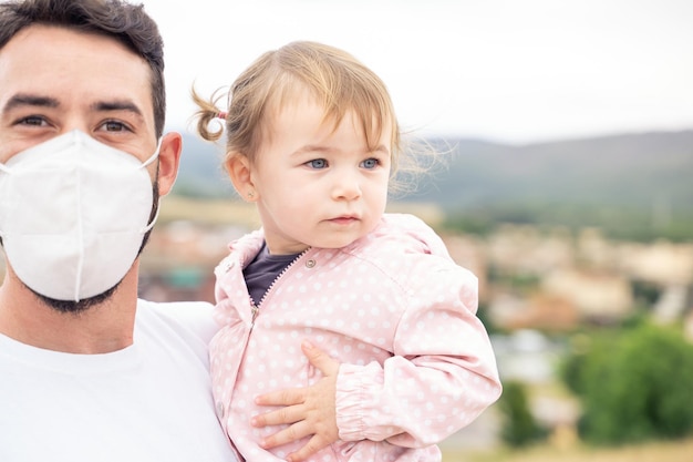 Father with protective facial mask holding a little girl outdoors