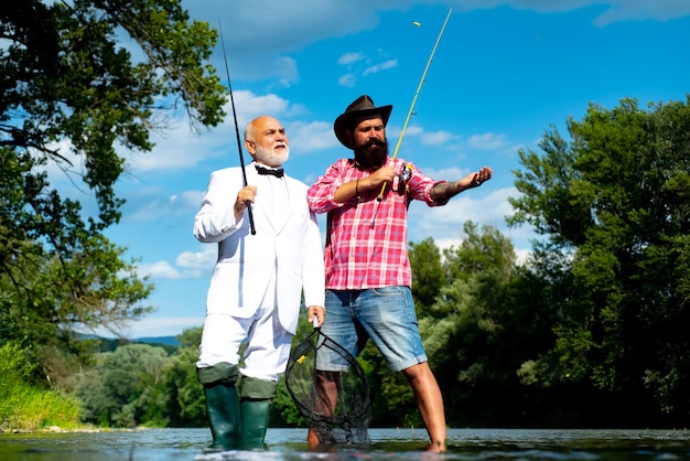 Father with son on the river enjoying fishing holding fishing rods portrait of cheerful two bearded ...