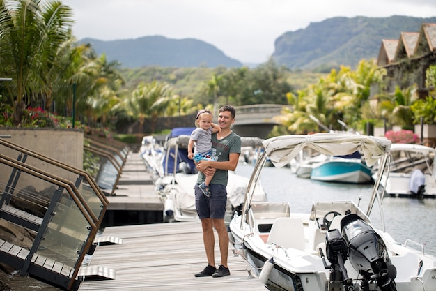 Father with son sitting on the sea pier. Happy dad and son are walking, looking at boats.