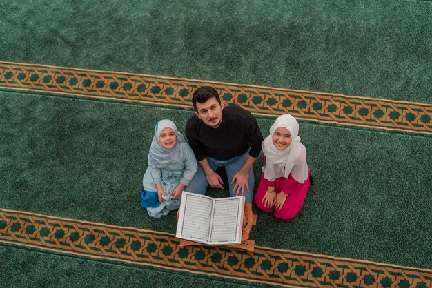 모스크 행복한 이슬람 가족 안에서 거룩한 책 꾸란을 읽는 두 자녀를 둔 아버지