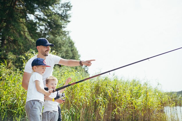 Отец с двумя маленькими сыновьями ловит рыбу на озере летом по выходным.