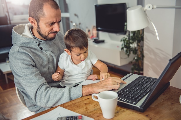 father working on laptop and holding son on his lap