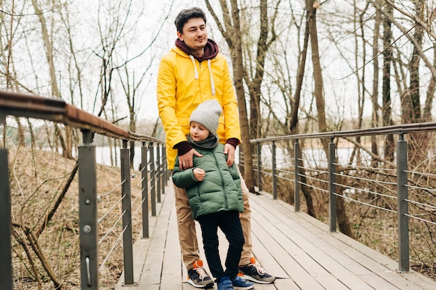 Padre in impermeabile giallo e figlio che si divertono nella foresta famiglia felice con un bambino che gioca e