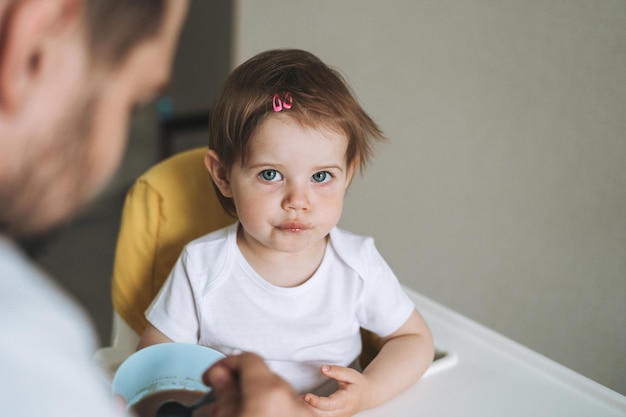 Father young man feeds baby girl little daughter in kitchen at home