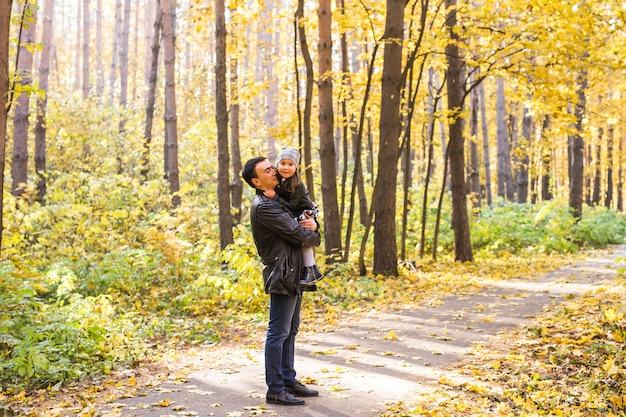 父性、子供、家族の概念-秋の公園で娘を抱いている父。