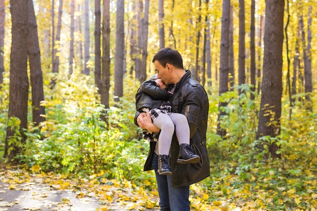 Fatherhood, family and leisure concept - father holding little daughter in his arms in autumn park