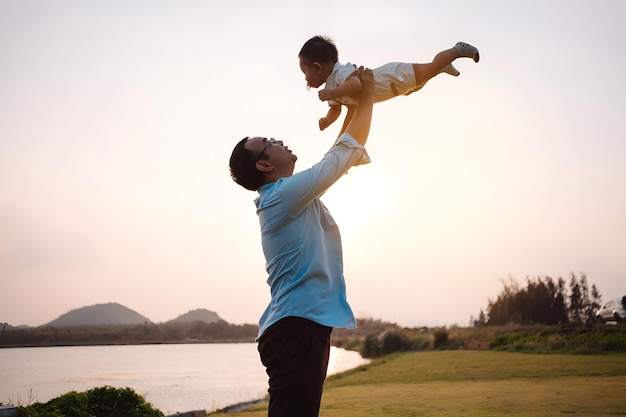 Foto la paternità solleva il figlio bambino che si diverte nel parco vicino al fiume al tramonto