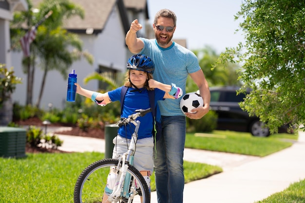 Foto concetto di festa del papà padre e figlio nel casco da bici che imparano il giro in bicicletta la famiglia sportiva ha eccitato il padre