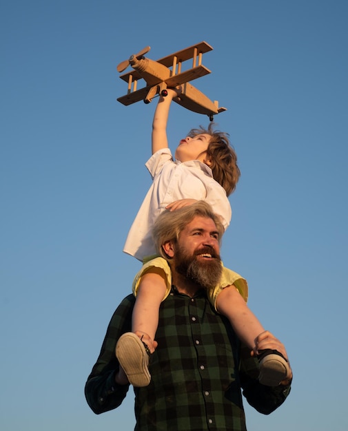 Fathers day father and son boy with toy aeroplane sitting on fathers shoulders on sky