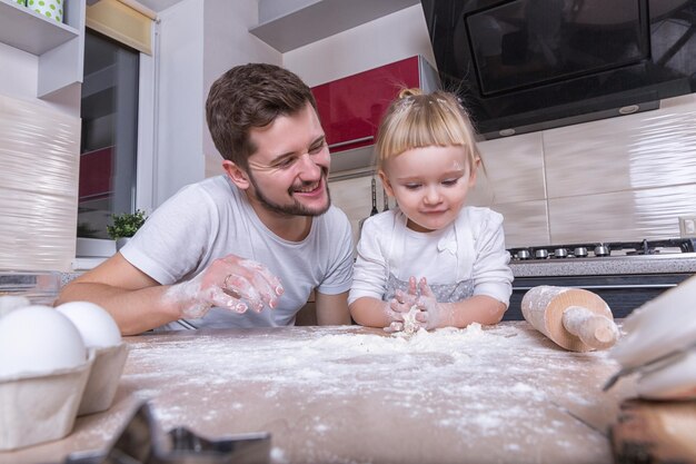 父の日ブロンドの髪の小さな甘い女の子は、キッチンで料理をしている彼女のお父さんと一緒に時間を過ごします