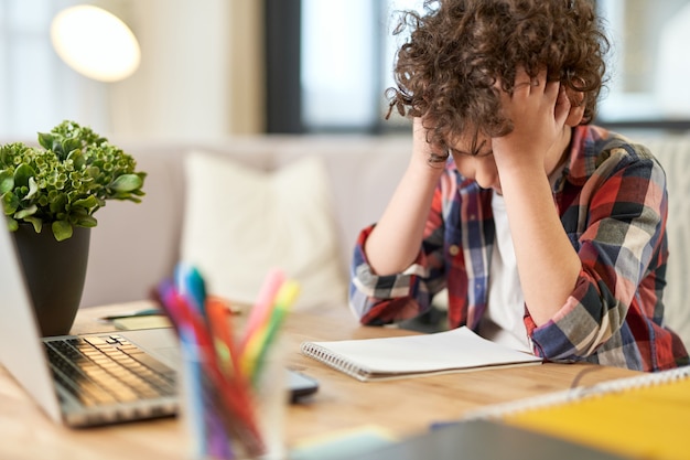 Fatigue portrait of tired latin boy holding his head looking sad while sitting at the