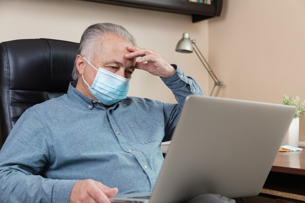 Fatigue senior man in face mask working or communicate on laptop at home. study, training, work, communication, entertainment, leisure during the coronavirus period.