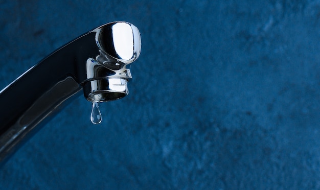 Faucet and water drop close-up on blue background. Water consumption concept