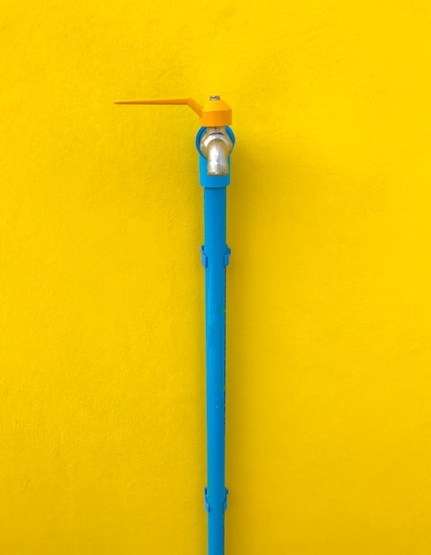 Faucet with blue water pipe on yellow wall.