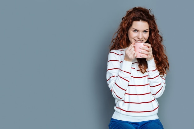 Favoriete drankje. Vrolijke blije aardige vrouw die glimlacht en een kop houdt terwijl het hebben van thee