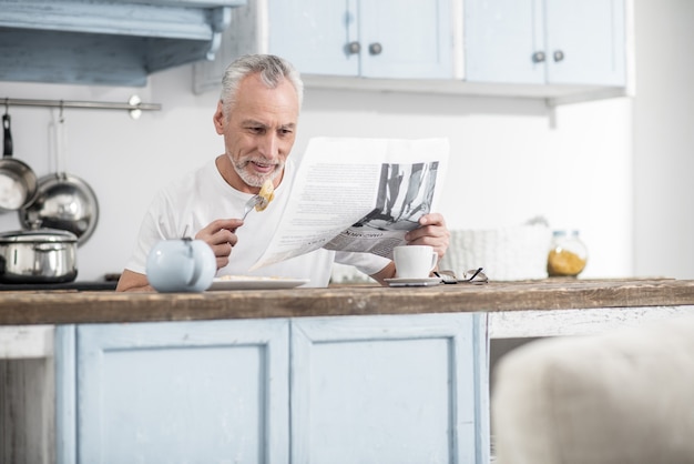 Favoriete eten. Vrolijke man positiviteit uiten tijdens het lezen van artikel en het eten van omelet