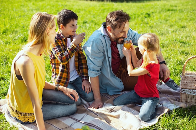 Favoriete sap. Vrolijke donkerharige papa die lacht en wat sap drinkt met zijn kinderen