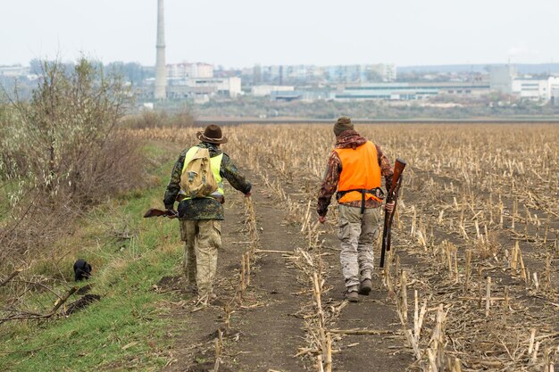 Fazantjagers die met jachtgeweer door een weide lopen.