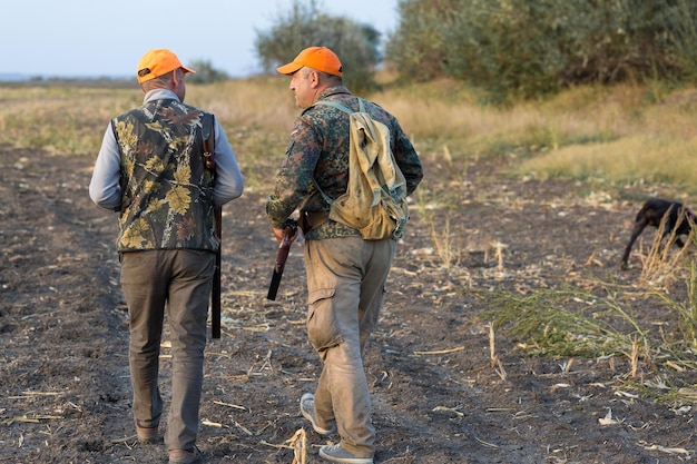 Fazantjagers die met jachtgeweer door een weide lopen.