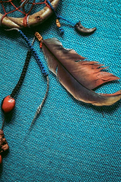 A feather is laying on a turquoise cloth with a stone and a stone on the right side.