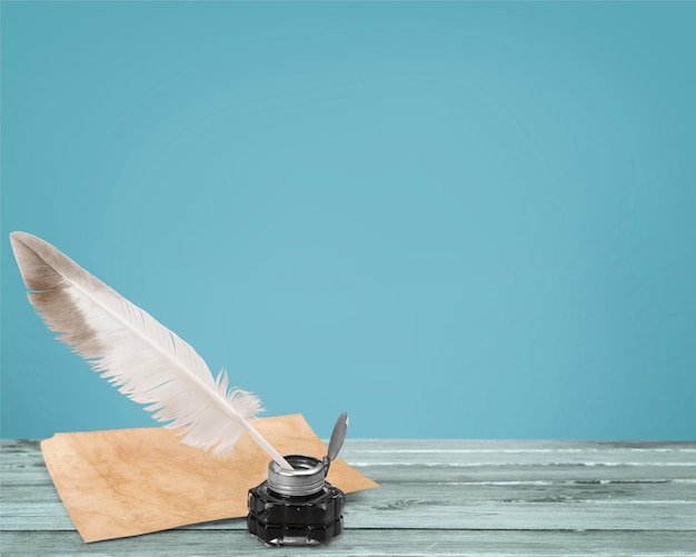 Feather quill pen and glass inkwell on library background