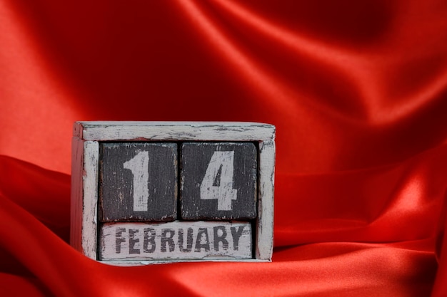 Photo february 14 on wooden calendar on background of red silk fabric valentines day