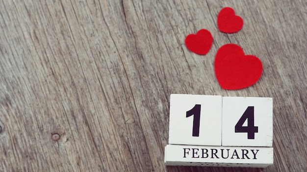 Photo february 14 on wooden cube calendar, on blurred wooden table with red hearts